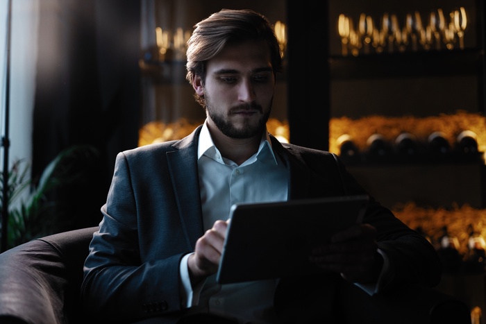 Hombre de negocios trabajando en una tableta mientras est&aacute; sentado junto a la ventana en un caf&eacute; a altas horas de la noche
