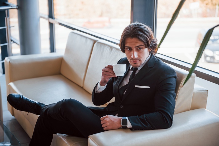 portrait handsome young businessman black suit tie that sits sofa takes break