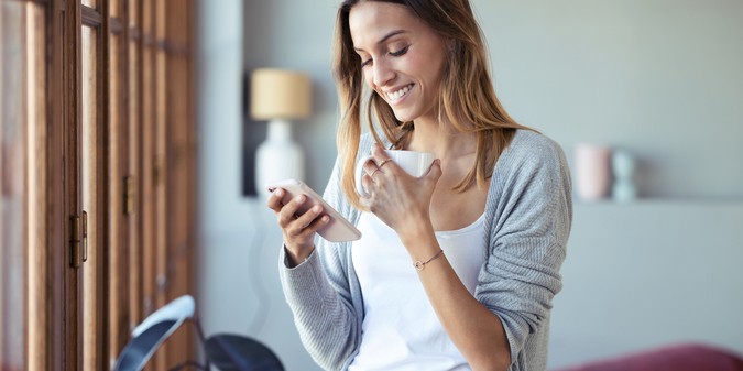 woman using her mobile phone while drinking coffee